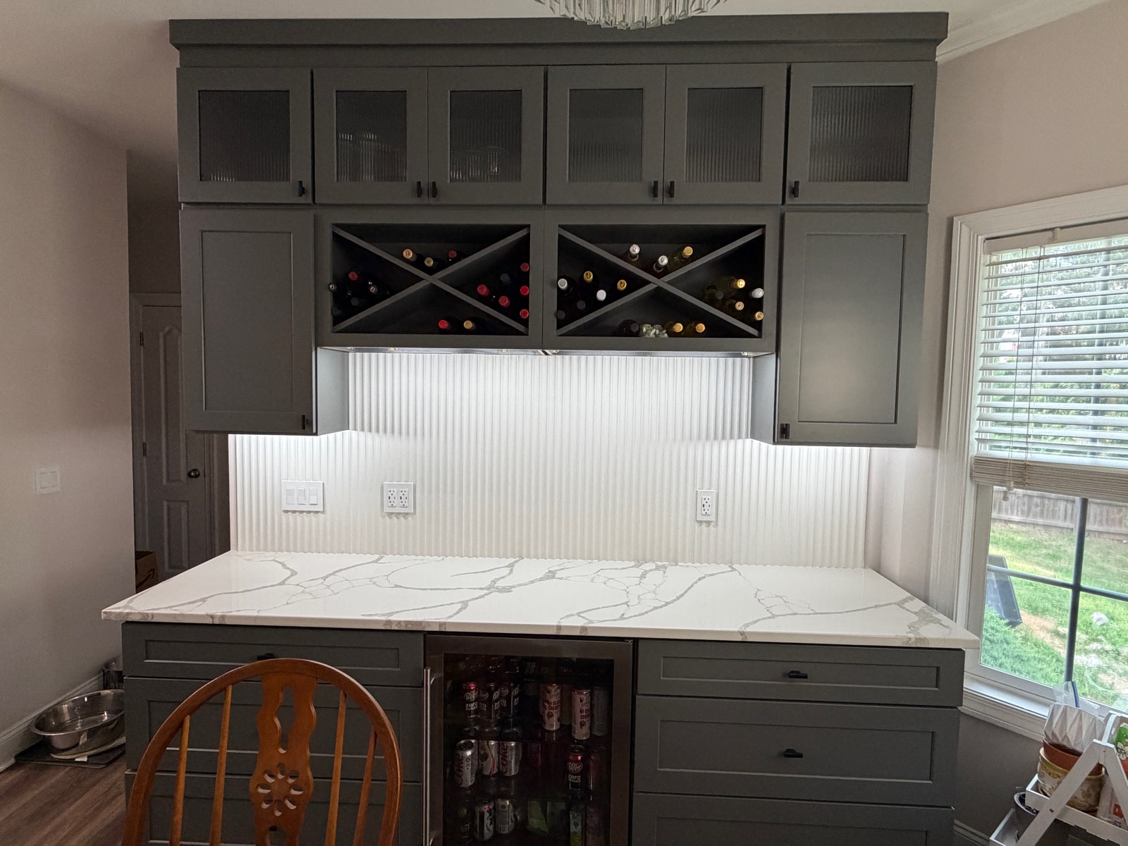 Butler&rsquo;s pantry with grey cabinetry, glass uppers, an X wine rack, quartz counter, and beverage fridge.