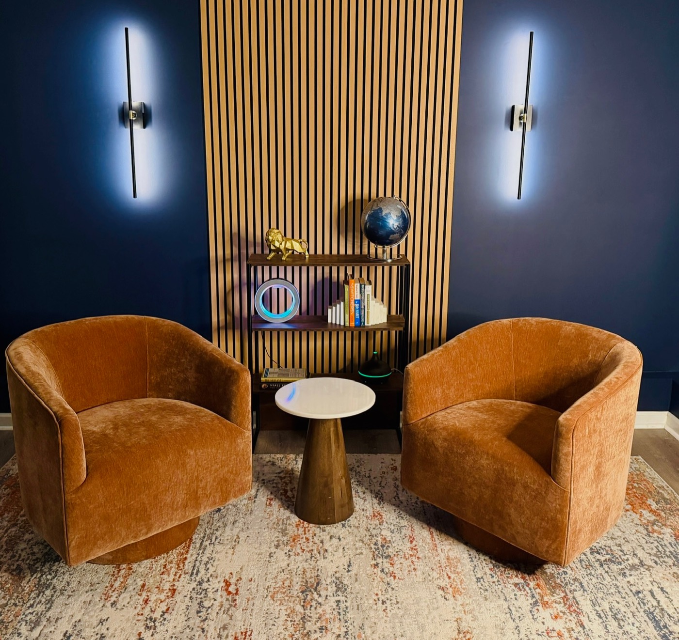 Sitting room with navy painted walls, a wood slat feature wall, wall sconces, and wide-plank flooring.