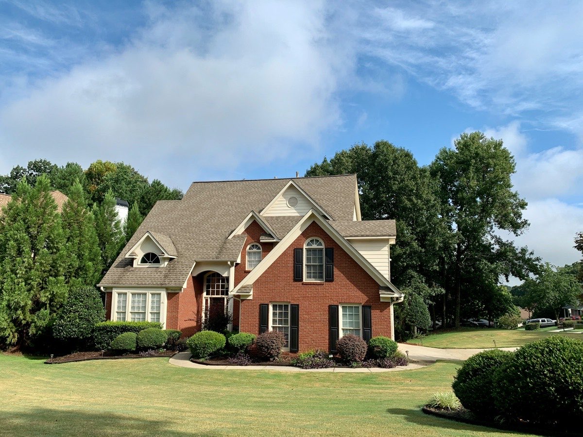 Brick and siding two-story house with a landscaped front lawn and mature trees.