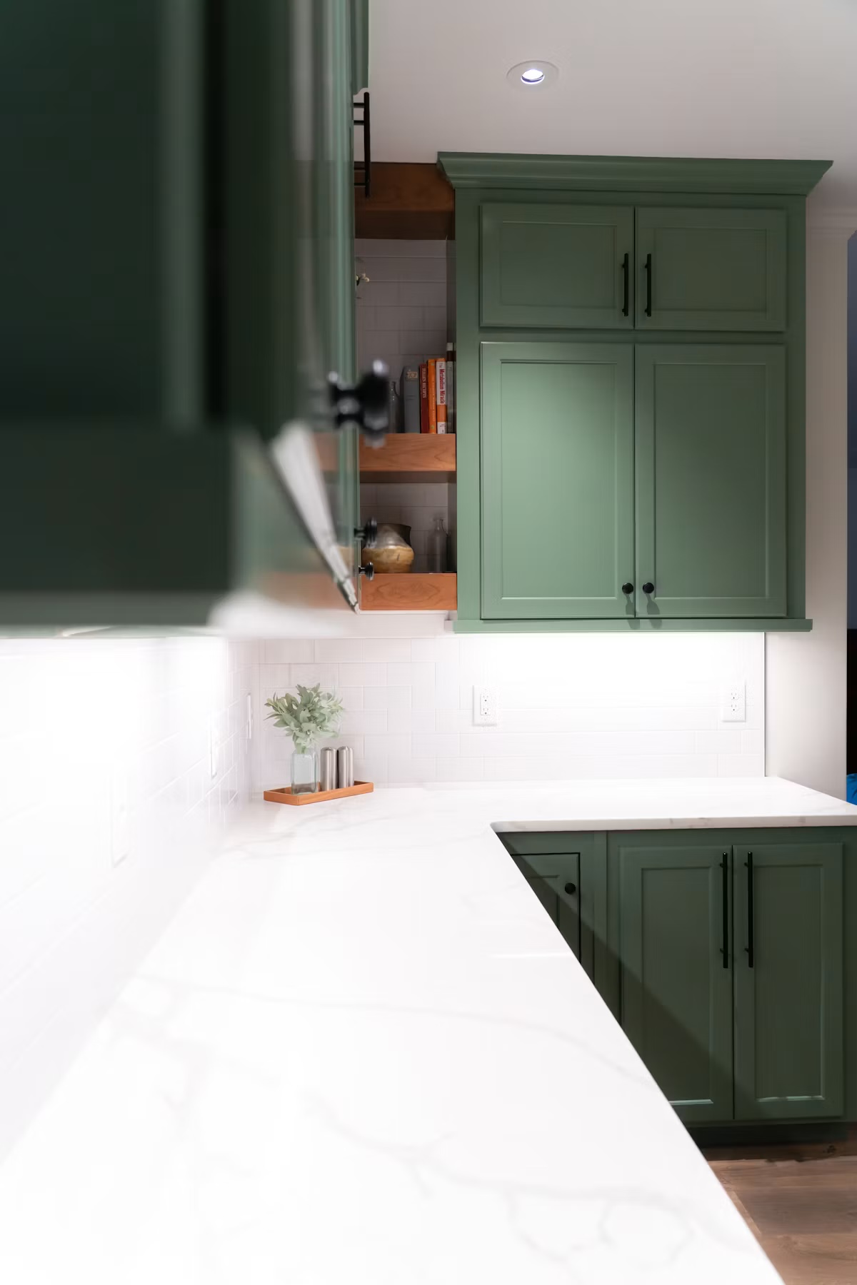 Kitchen with deep green shaker cabinets, black hardware, a white subway tile backsplash, and a marble waterfall countertop.