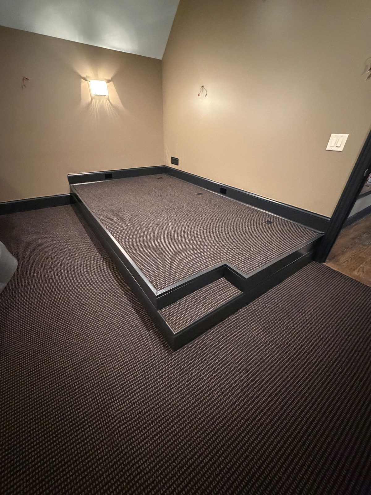 Carpeted seating riser framed in dark trim, built into a bonus room under a sloped ceiling.