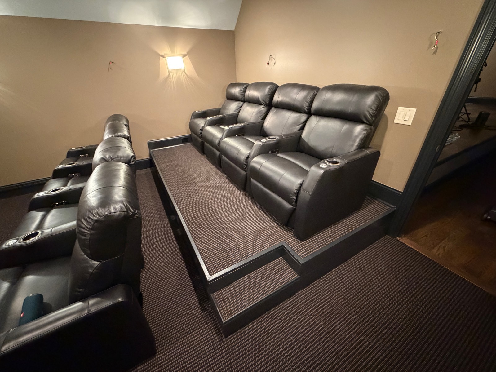 Home theater seating on a carpeted riser, with wall sconces and dark trim.